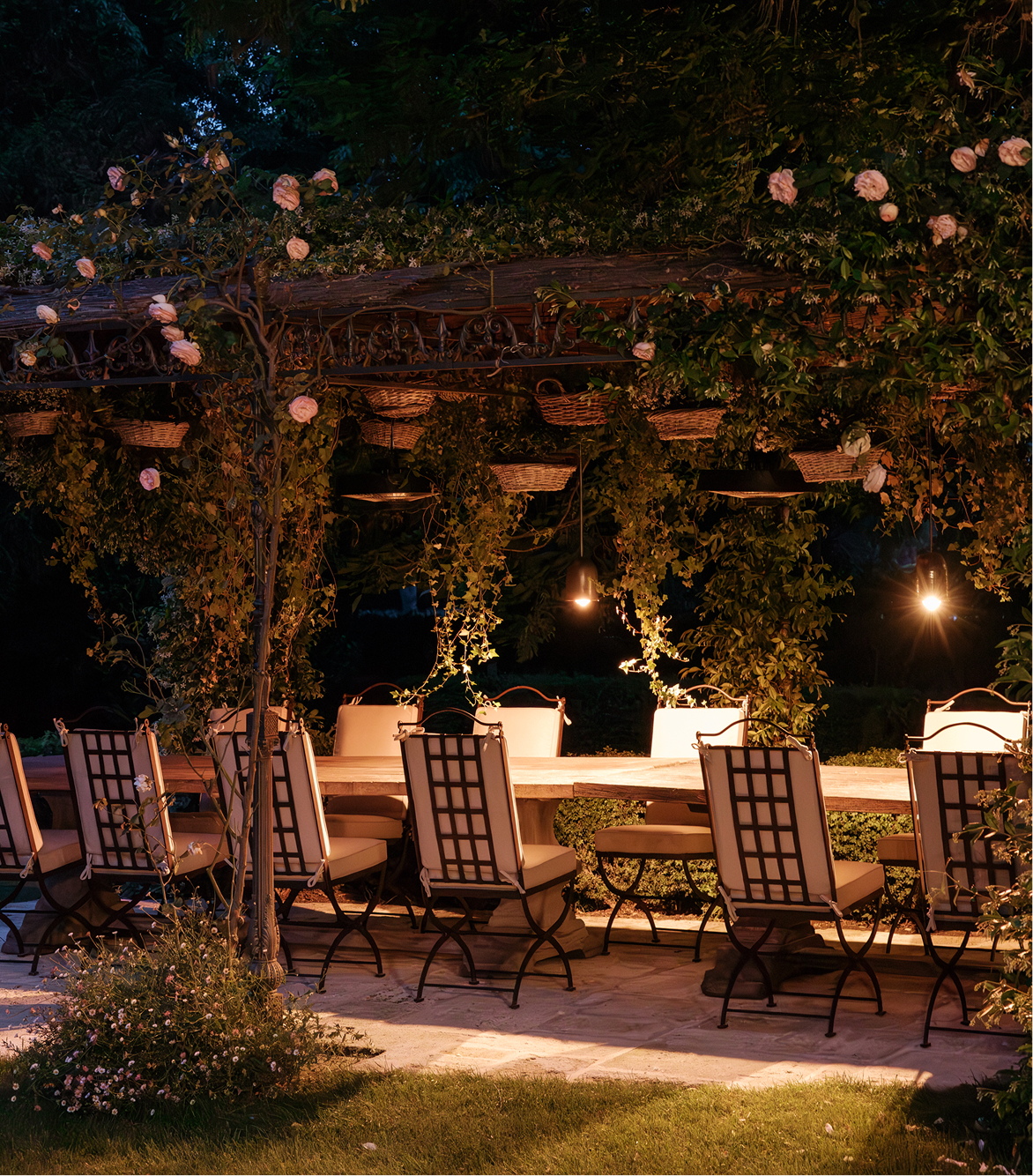 Evening dining beneath a flower-covered pergola, featuring Hervé Baume HB1 Quadrillage Collection wrought-iron outdoor furniture.
