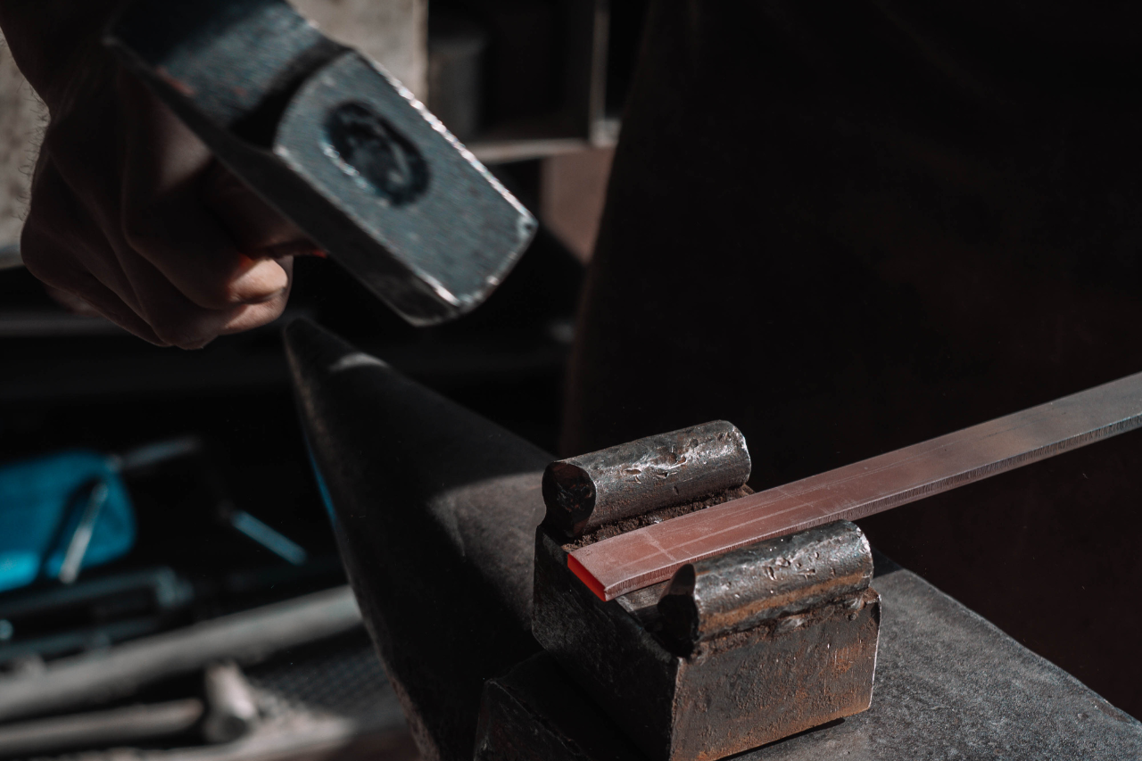 Craftsman shaping metal by hand with a hammer in the Hervé Baume ironworking workshop.